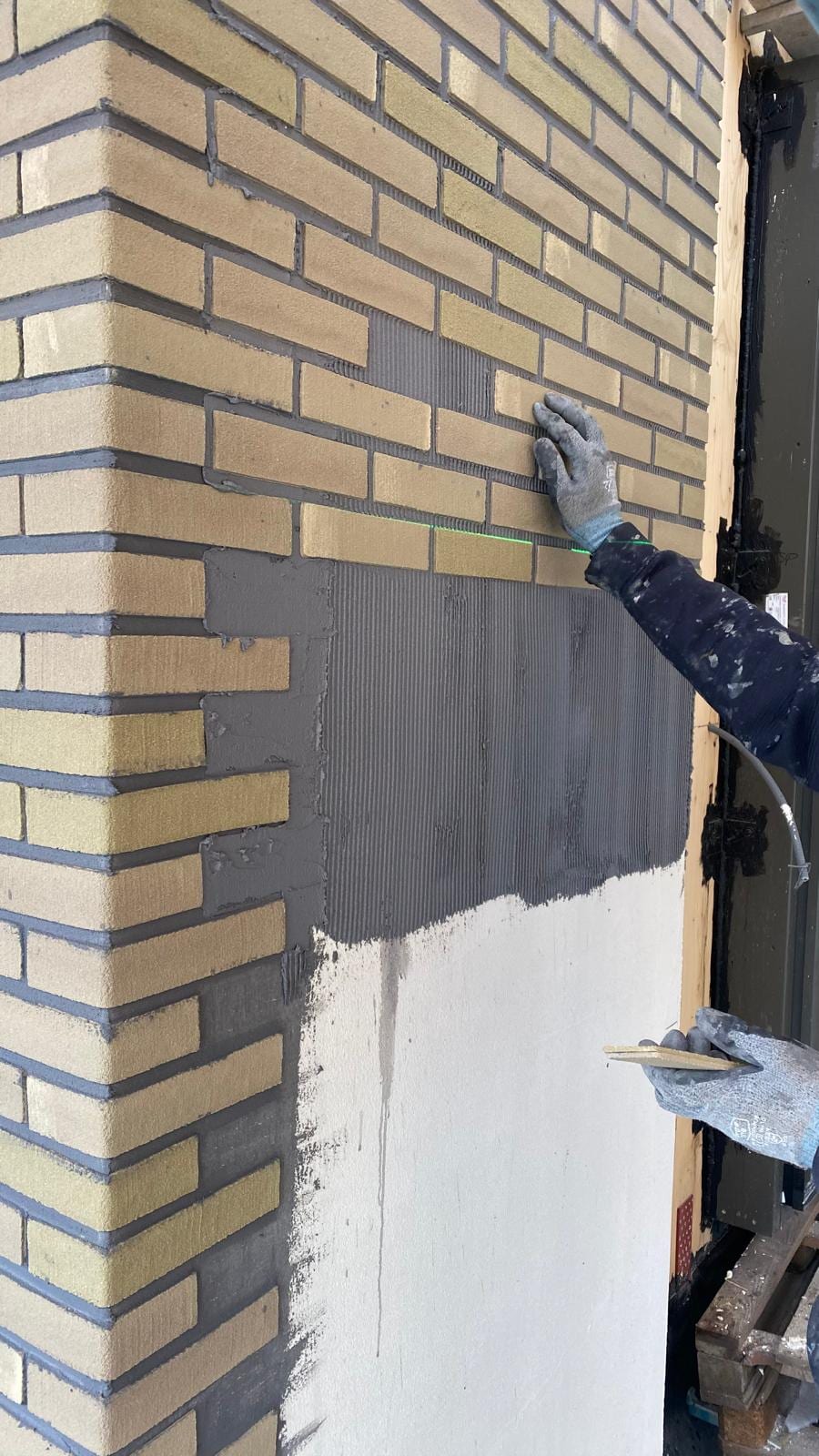 Vakman zet lichte minerale gevelstrips in een grijs lijmbed en strijkt de voegen direct af