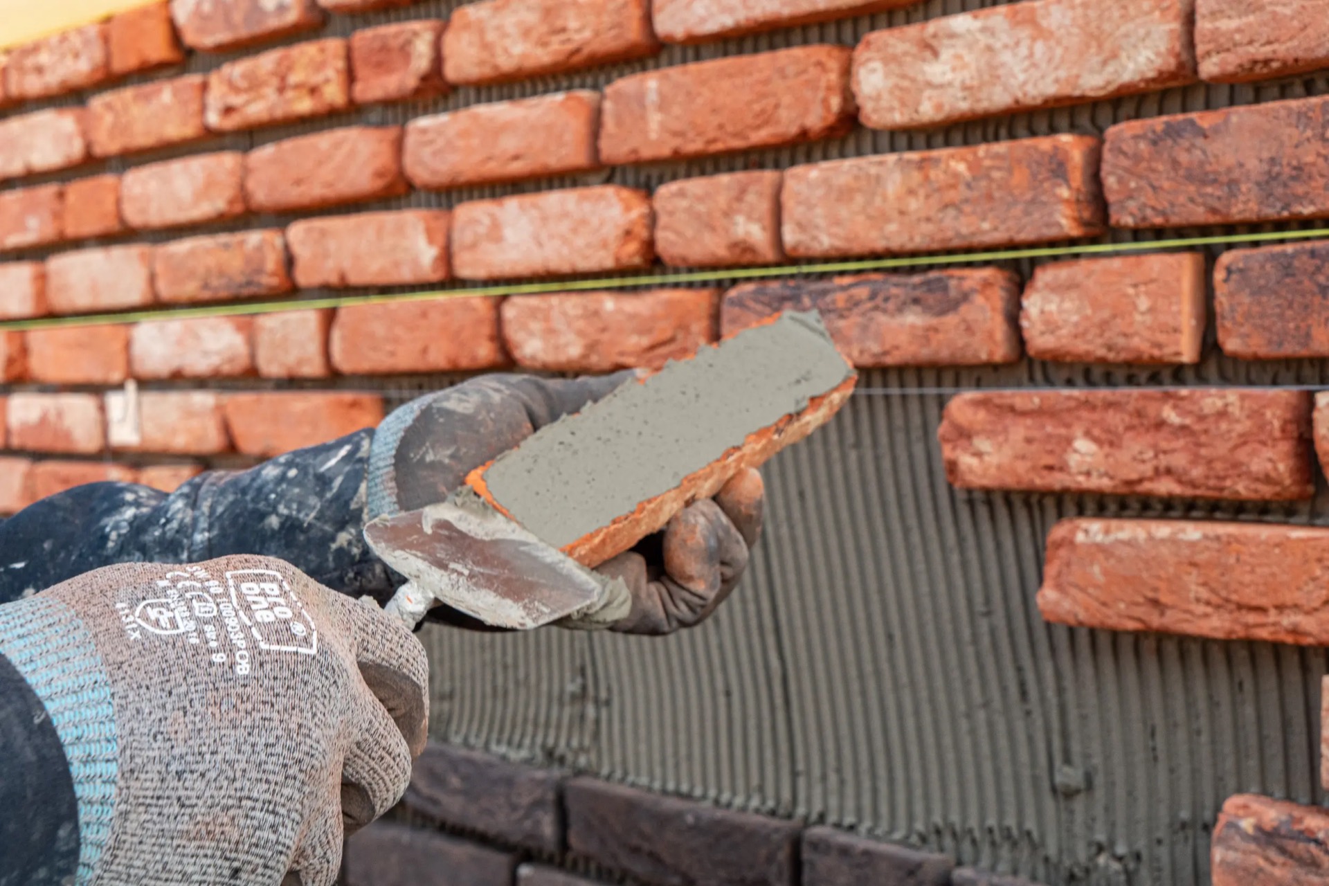 Vakman van IBS Afbouw verlijmt een steenstrip op een gevel met isolatie en lijmlaag