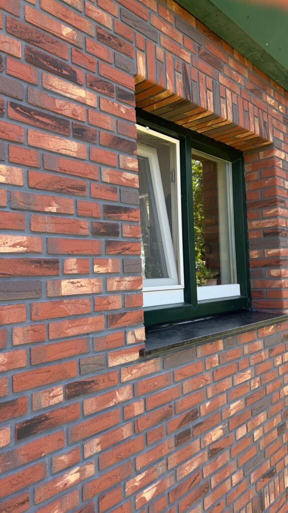 Raam in een gevel van rode minerale steenstrips met donkergroen kozijn