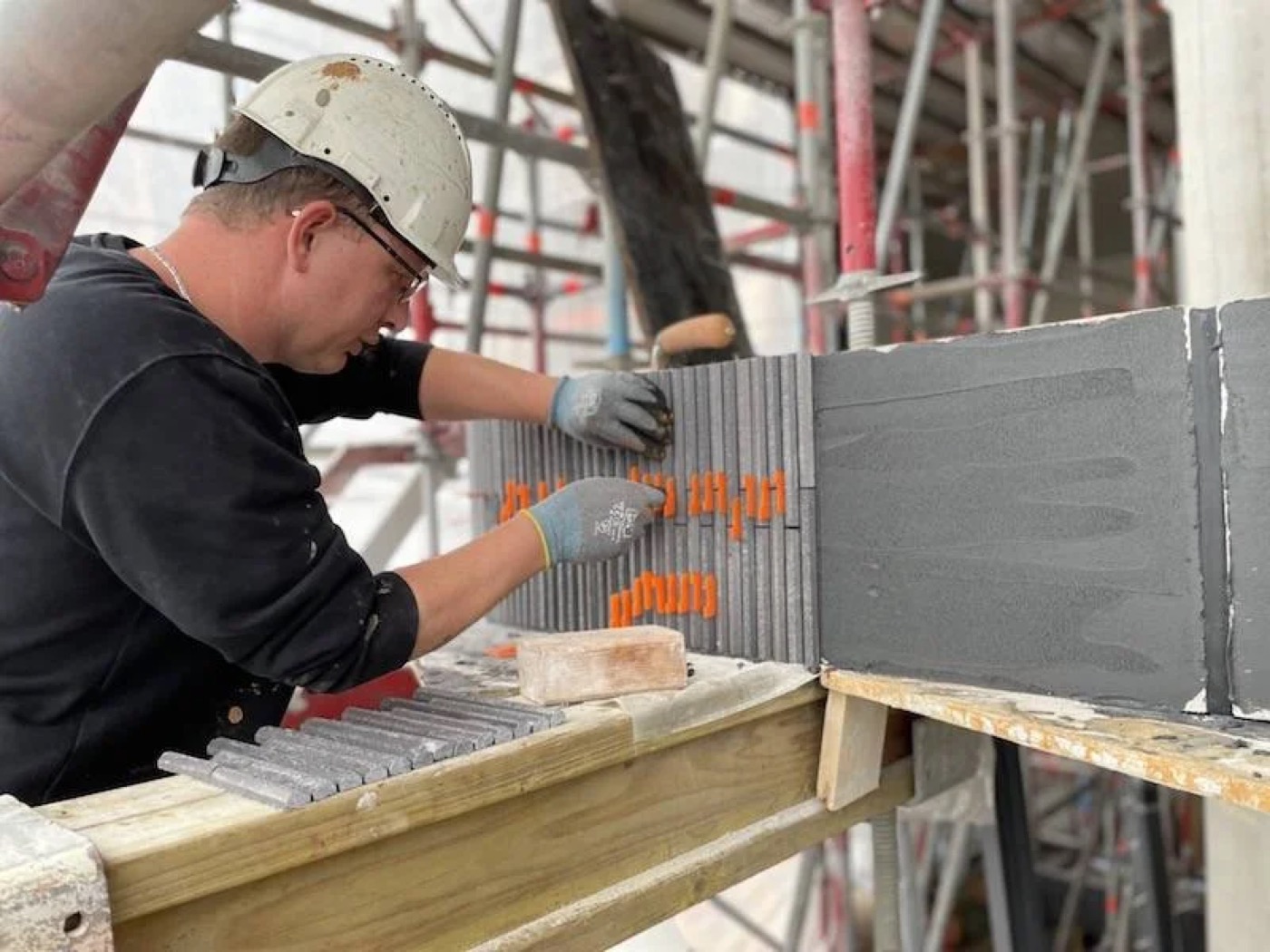 Vakman van IBS Afbouw verlijmt grijze steenstrips op een paneel in de steigers bij project De Hoogh in Amsterdam
