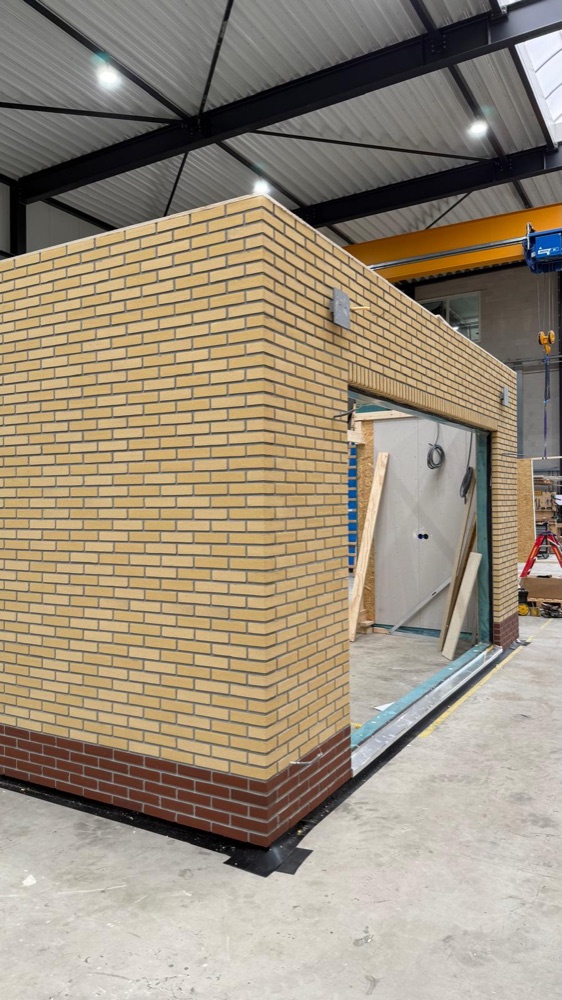 Prefab aanbouw met gele minerale steenstrips en een donkere plint in de werkhal
