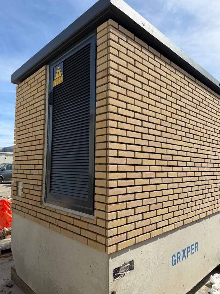 Trafostation met gele steenstrips en een donkere ventilatiedeur