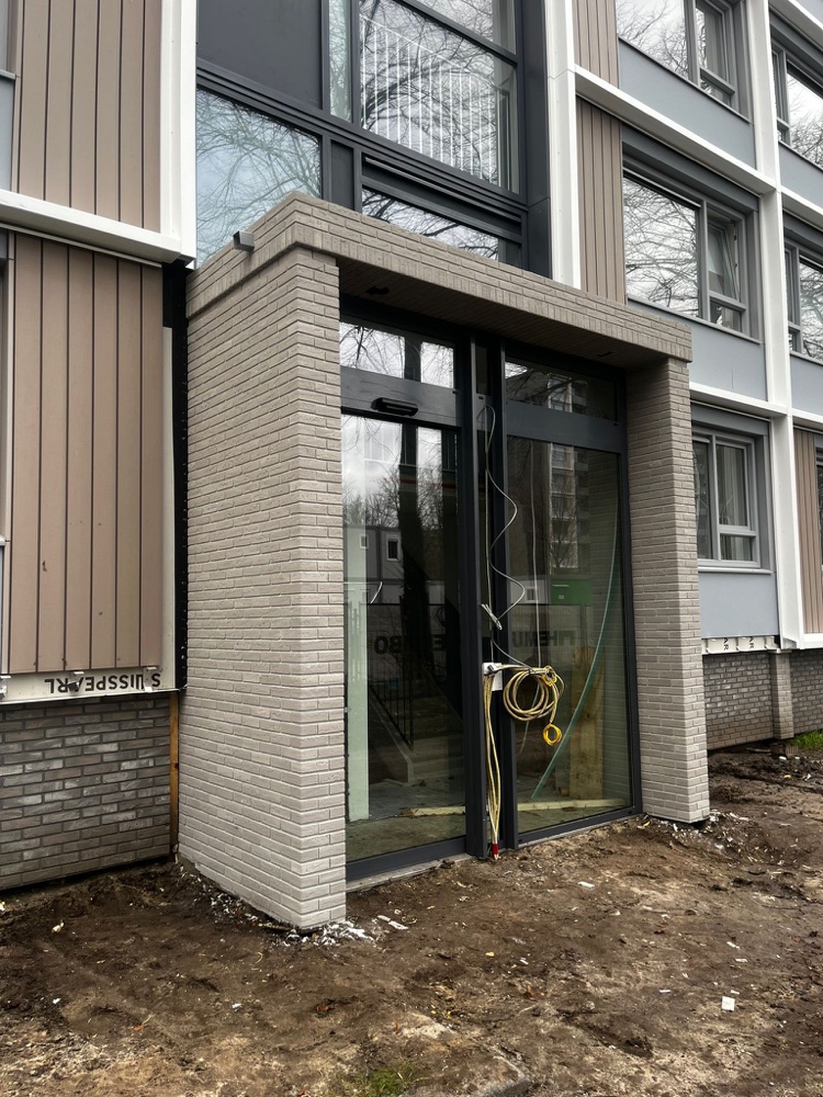 Traphuis-entree in Utrecht met een omlijsting van lichtgrijze minerale steenstrips en glazen deuren, schuin van opzij