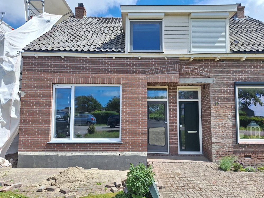 Voorgevel van de woning in Breezand tijdens het aanbrengen van de steenstrips, met nieuwe kozijnen