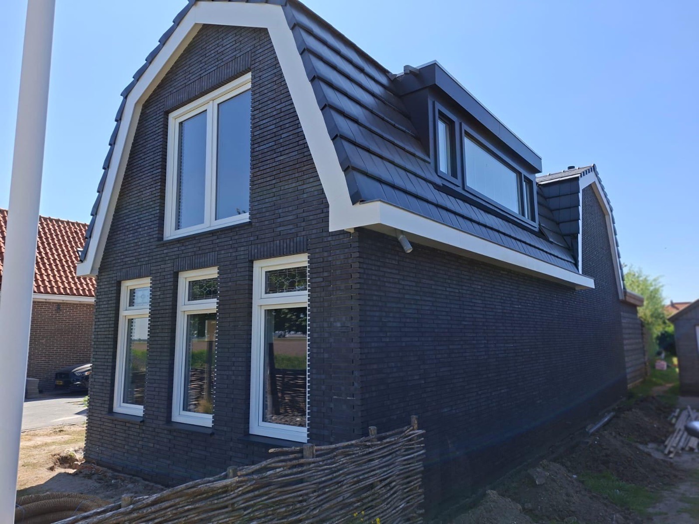 Woning met mansardekap in Julianadorp, bekleed met donkere steenstrips, met witte kozijnen en een witte dakrand