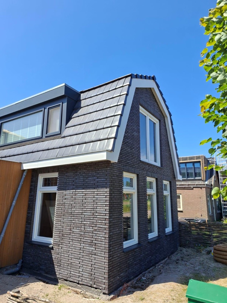 Hoek van de woning in Julianadorp met donkere steenstrips, witte kozijnen en de mansardekap