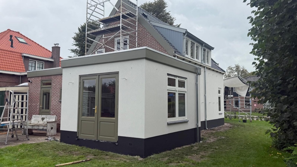 Andere zijde van de woning in Spanbroek met witte sierpleister, een donkere plint en de steiger nog deels aanwezig