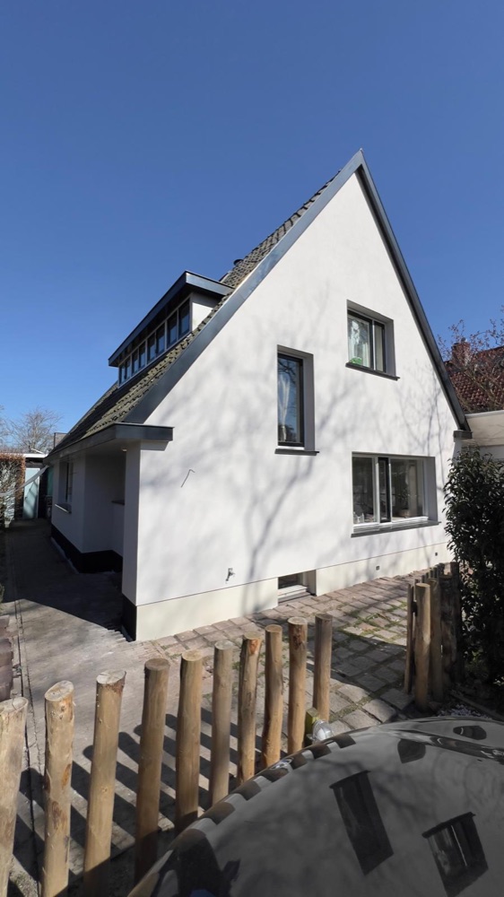 Zijgevel van het woonhuis in Bergen met witte sierpleister onder een blauwe lucht