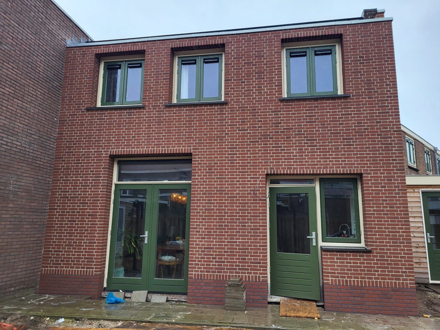 Gevel van een woonhuis in Haarlem met rode minerale steenstrips, groene deuren en drie ramen op de verdieping