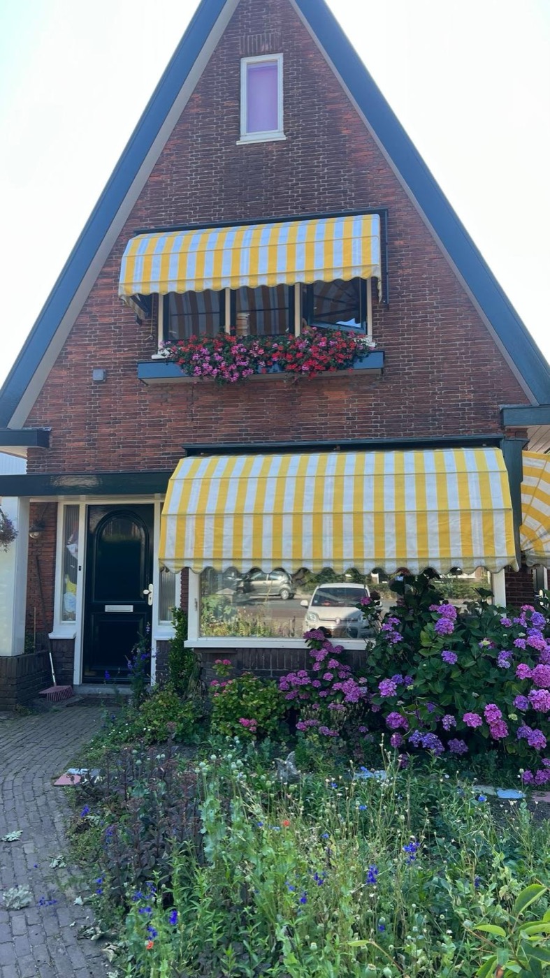Woonhuis in Heiloo met puntgevel en erker na de renovatie, met een gevel van rood-oranje steenstrips en een bord van IBS Afbouw in de voortuin